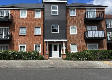 A three-storey block of brick-built flats with a dark weatherboarded stair tower, white windows, black balconies and planting along the front.