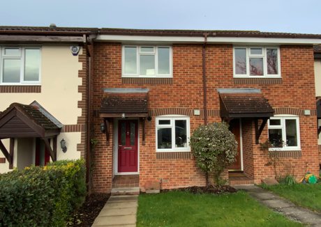 A brick-built terraced house with a red front door under a small tiled canopy, white windows and a small front lawn.