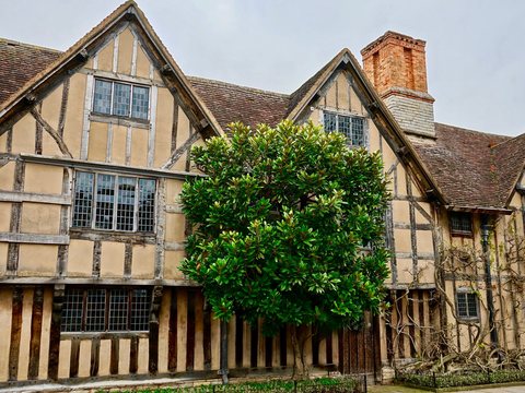 A historic close-studded timber-framed building with a jettied upper floor, gabled roofs, leaded casement windows and a tall brick chimney stack.