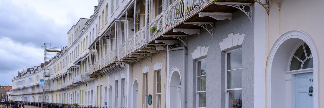 A long curving terrace of painted stucco houses with ironwork balconies, arched doorways and iron railings along the pavement.
